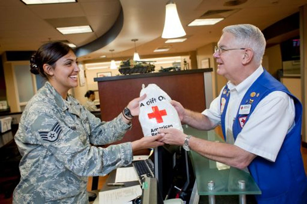 a Red Cross volunteer handing a Red Cross gift bag to a service member.