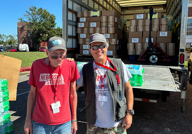Two Red Cross volunteers stand in front of a truck with disaster relief supplies