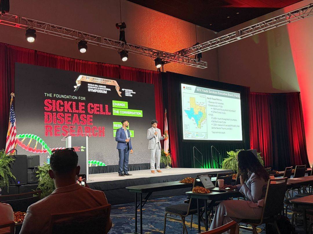 Two men stand on stage speaking for Sickle Cell research