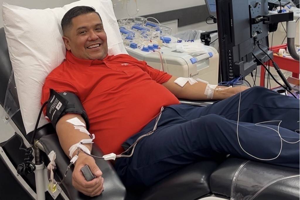 Man in red shirt donates platelets while smiling at camera