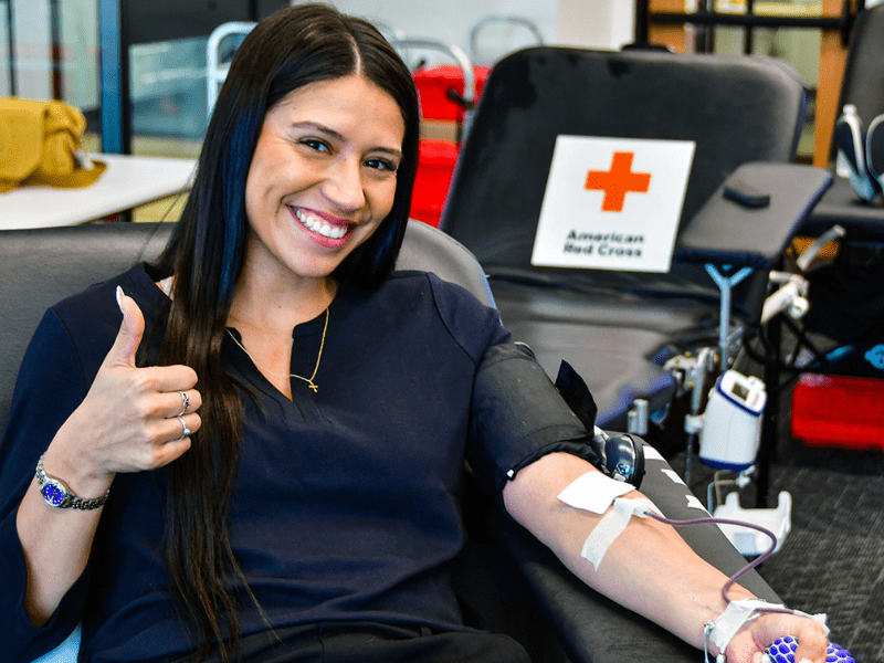Woman sitting in chair donating blood giving a thumbs up sign.