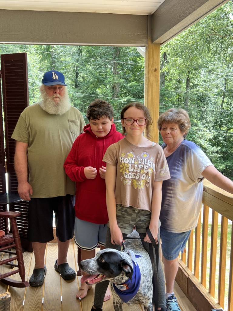 Family stands on front porch with dog