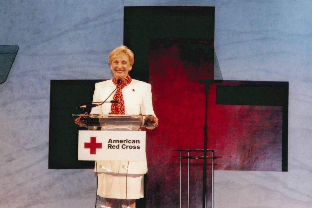 Woman stands at podium in front of Red Cross emblem