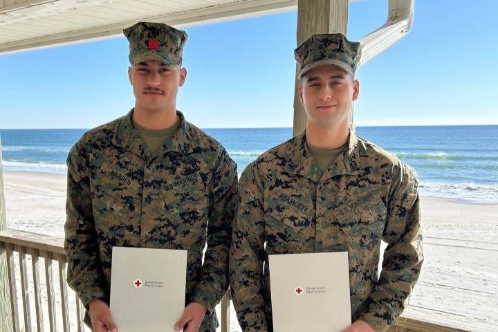 Two men in uniform stand holding Red Cross awards