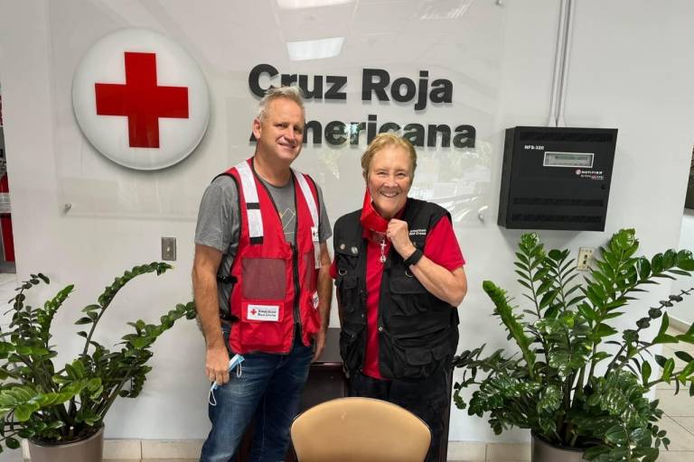 Male and female Red Cross volunteer stand behind table