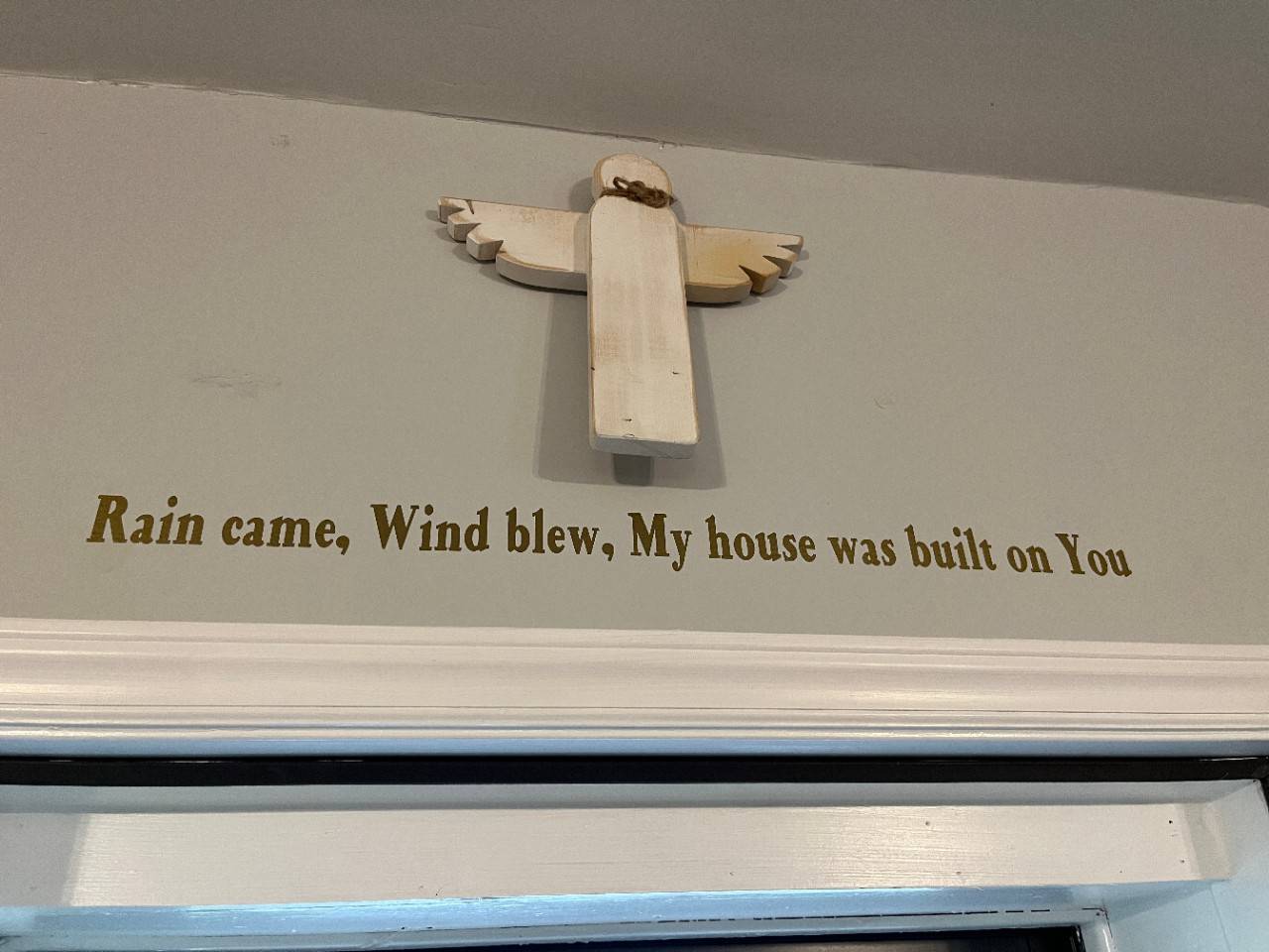 Quote on wall printed below wooden angel figurine