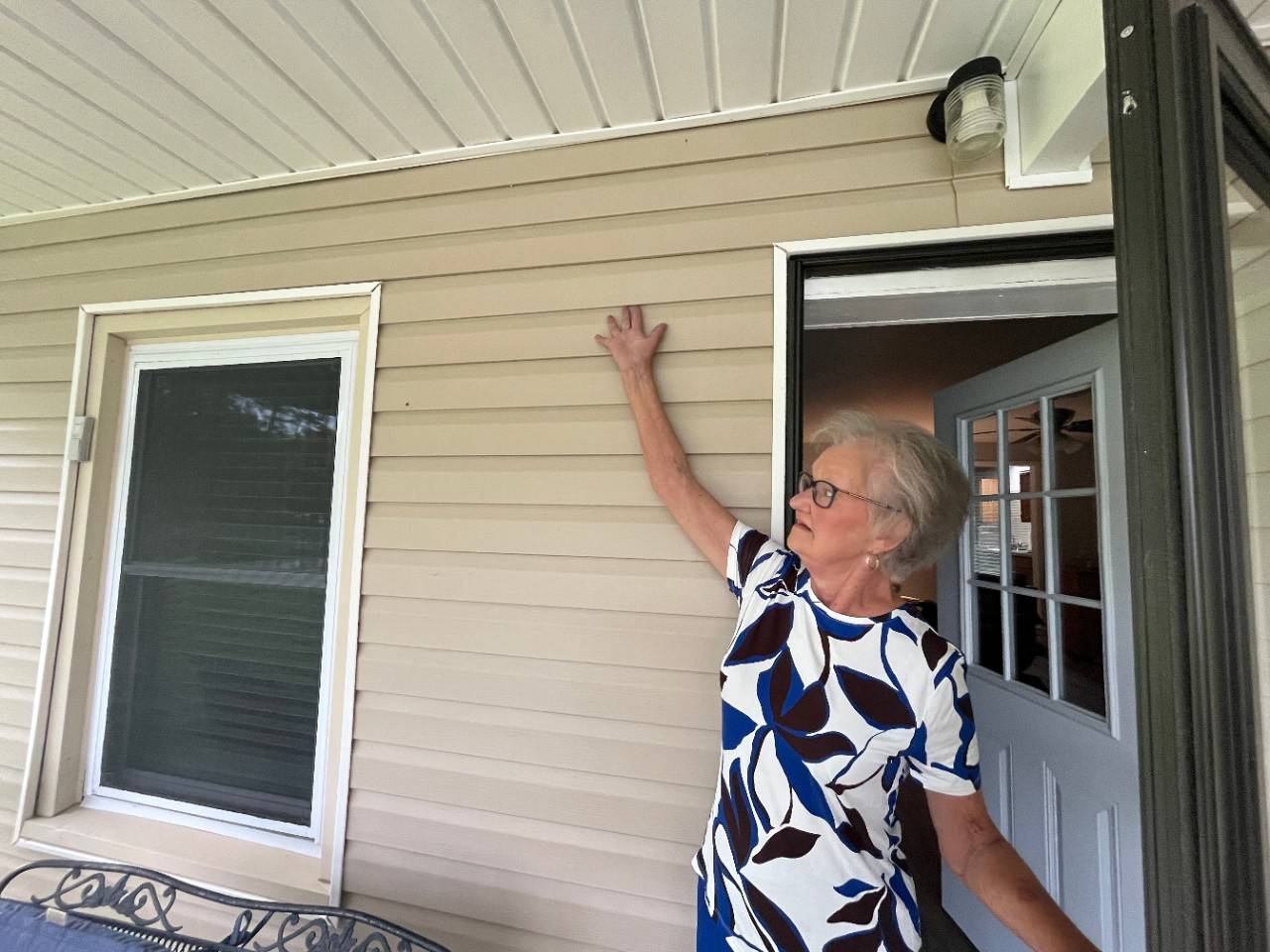 Woman stands outside front door while touching the side of her home