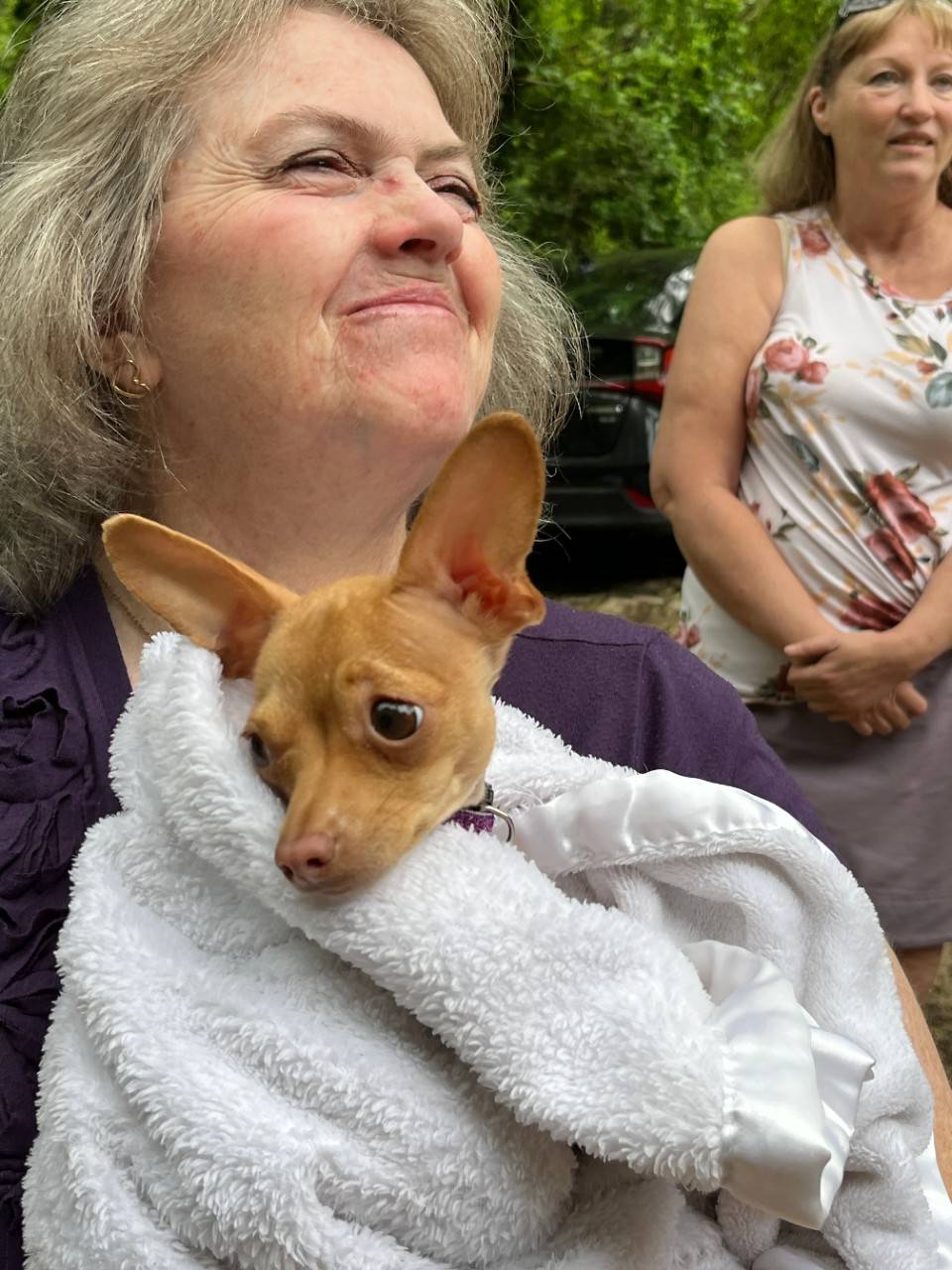 Woman holds small dog in a towel near her chest
