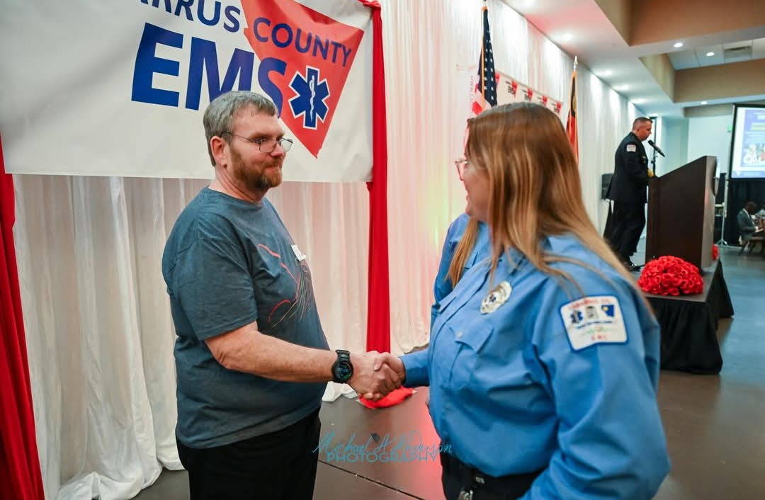 Man shakes hands with first responder in front of EMS sign