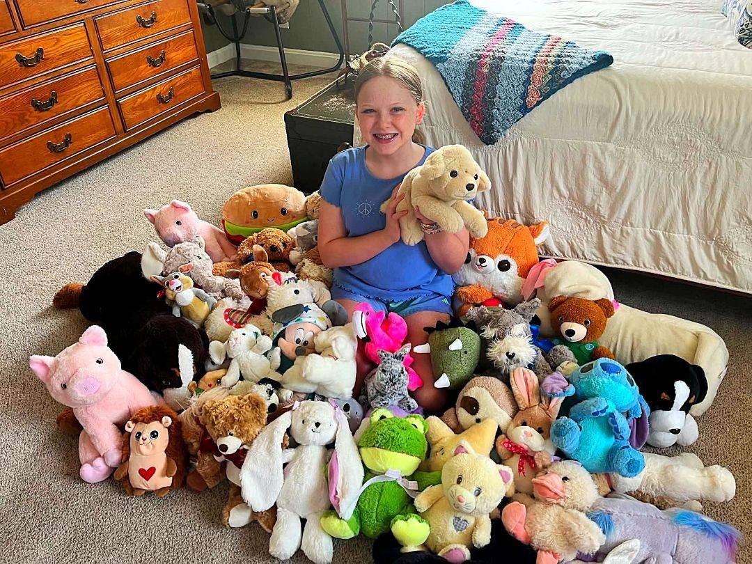 Young girl sits with dozens of stuffed animals