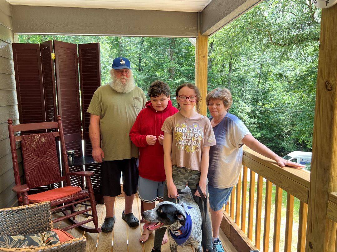 Family stands on front porch with dog