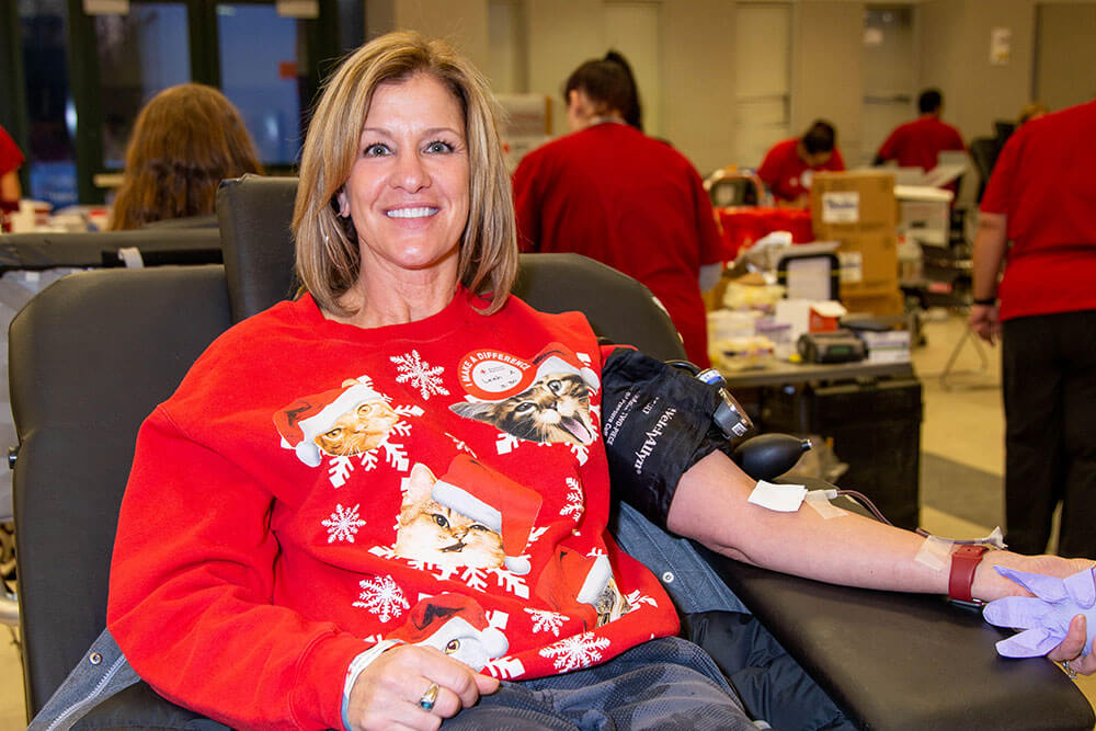 a person wearing a holiday sweater sitting in a chair donating blood.