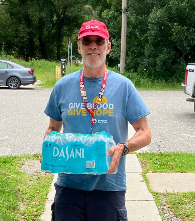Male Red Cross volunteer carries case of water