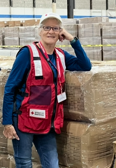 Woman in Red Cross vest leans against boxes