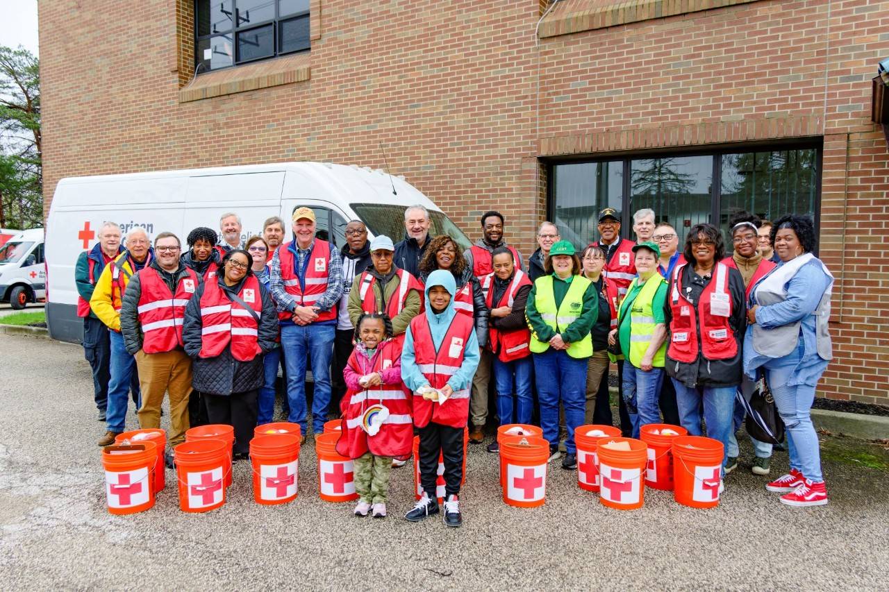 A group of Red Cross volunteers standing next to a Red Cross vehicle with buckets at their feet.