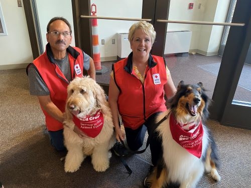 two red cross volunteers with two service dogs wearing red cross bandanas 
