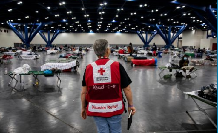 man in red cross vest in shelther with cots 