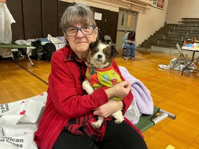 a woman in a red cross shelter holding her dog while sitting 