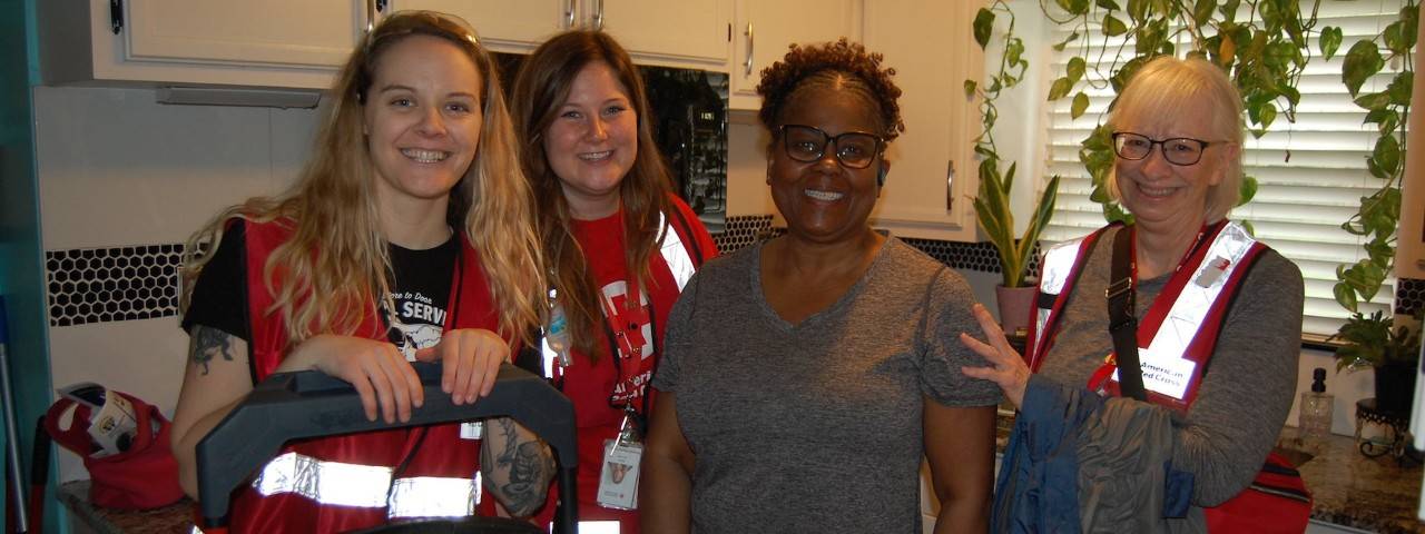 Group photo of four smiling femaile Red Cross volunteers wearing red vests and name badges