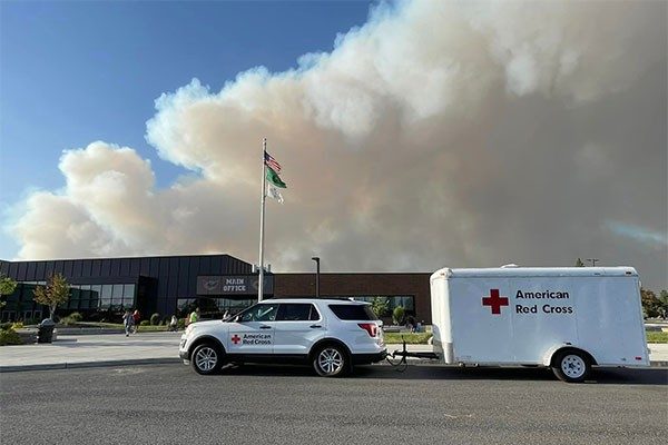 Red Cross vehicle with Smoke rising behind building from wildfire