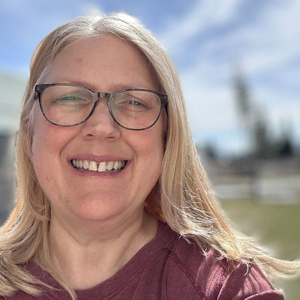 Deanna Whitson wearing glasses and smiling takes a selfie.