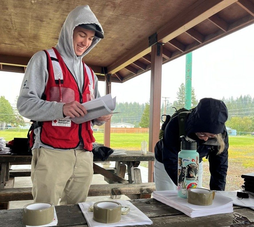 two red cross volunteers in red vest setting up tables