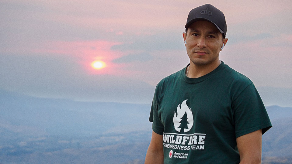 Wesley Clarillos stands on a hillside with a smoky setting sun in the background.