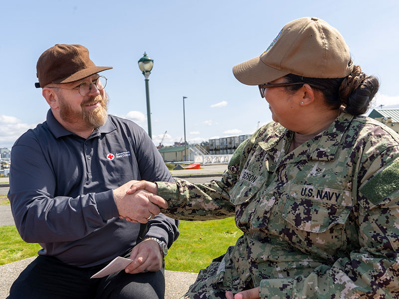 A Red Cross volunteer and a Military service member shaking hands.