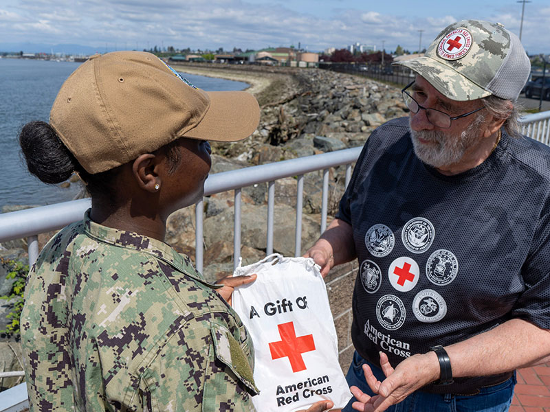 A military service member handing a Red Cross gift bag to a veteran.