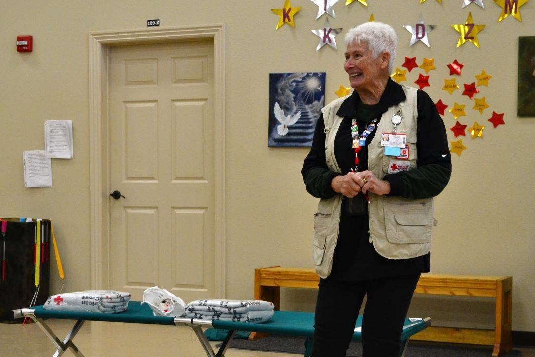 Woman stands in front of cot and red cross blankets