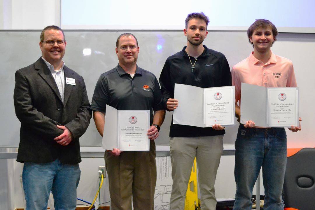 Four men stand in a row holding lifesaving awards