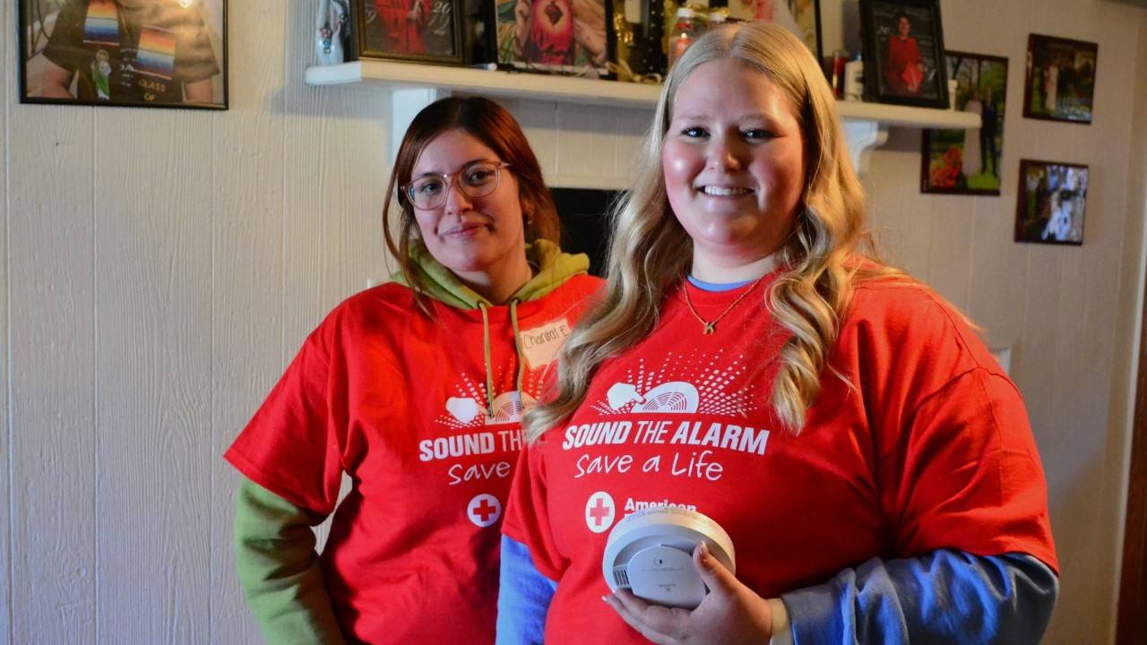 Red Cross volunteers getting ready to install smoke alarms pose in front of a house.
