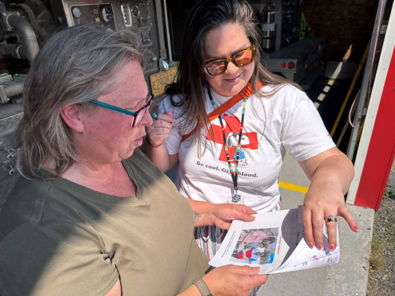 Woman in Red Cross tshirt shows brochure to woman in green shirt