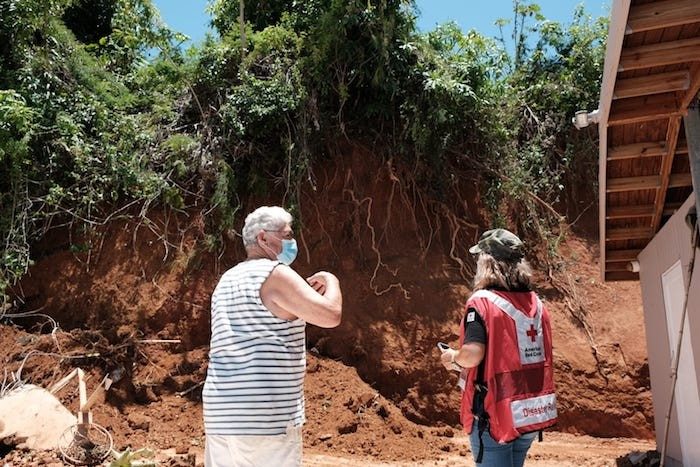 Red Cross volunteer and person wearing mask looking at crumbling hillside next to house