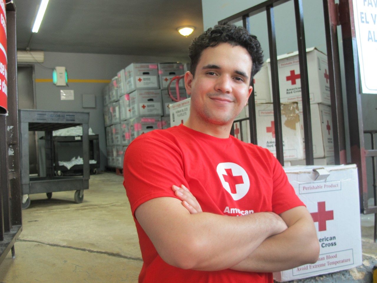 Voluntario con camisa de la Cruz Roja de pie frente al almacén de servicios de sangre.