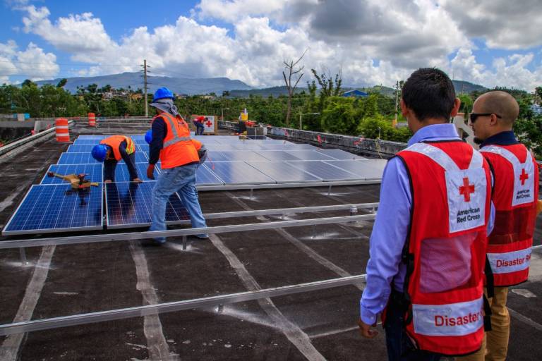 Fotografía de voluntarios de la Cruz Roja instalando paneles solares en un terreno.