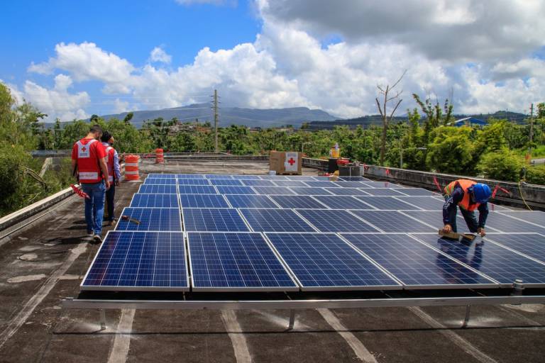 Fotografía de voluntarios de la Cruz Roja instalando paneles solares en un terreno.