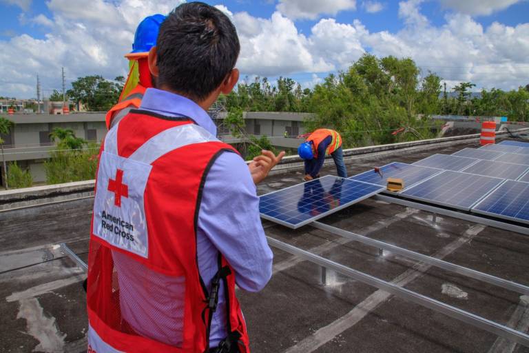 Fotografía de voluntarios de la Cruz Roja instalando paneles solares en un terreno.