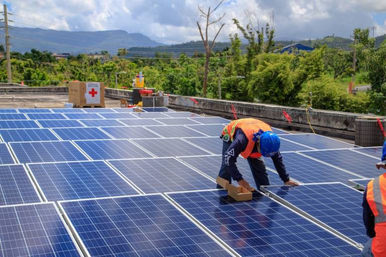 Fotografía de voluntarios de la Cruz Roja instalando paneles solares en un terreno.