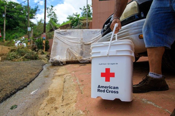 Persona afectada por unas inundaciones carga un cubo de limpieza de la Cruz Roja.