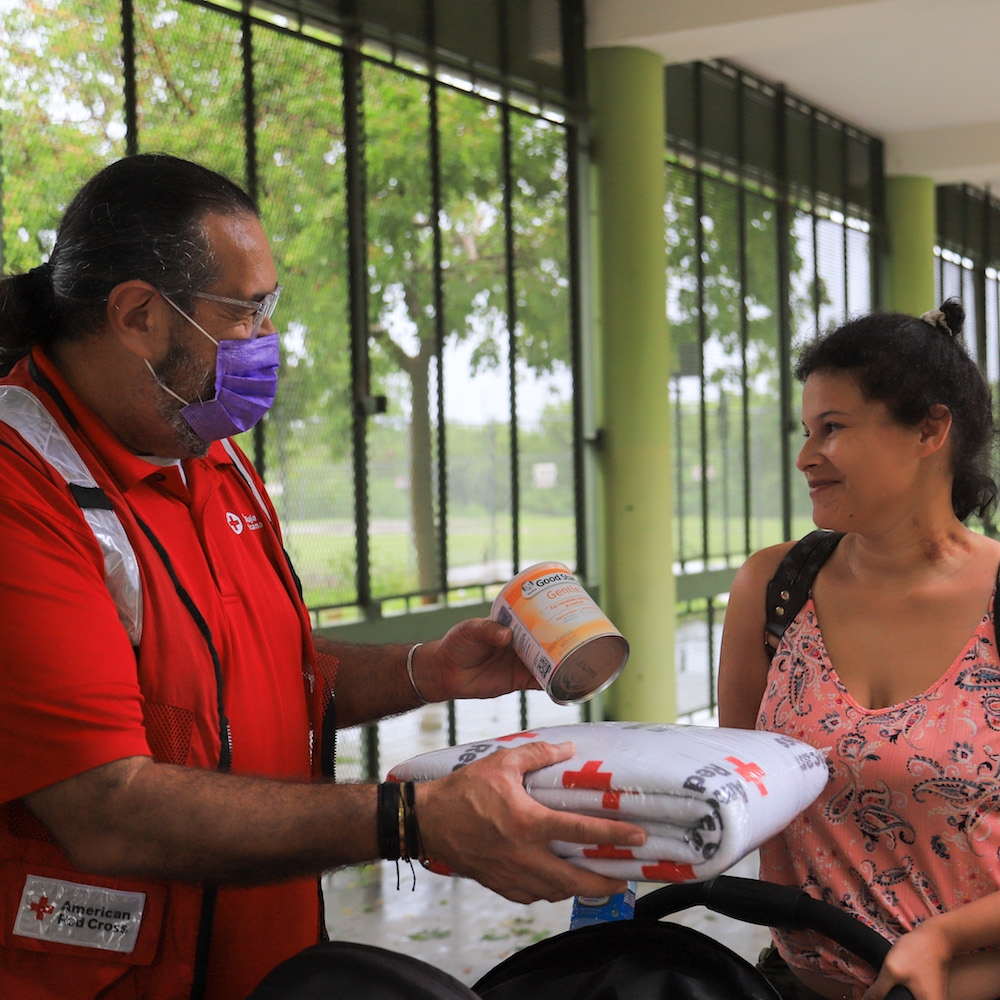 Personal de la Cruz Roja entrega fórmula de bebé y una manta a una residente del refugio luego del huracán Fiona en Salinas.