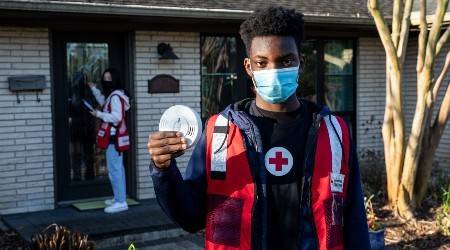 Red Cross volunteers getting ready to install smoke alarms pose in front of a house.