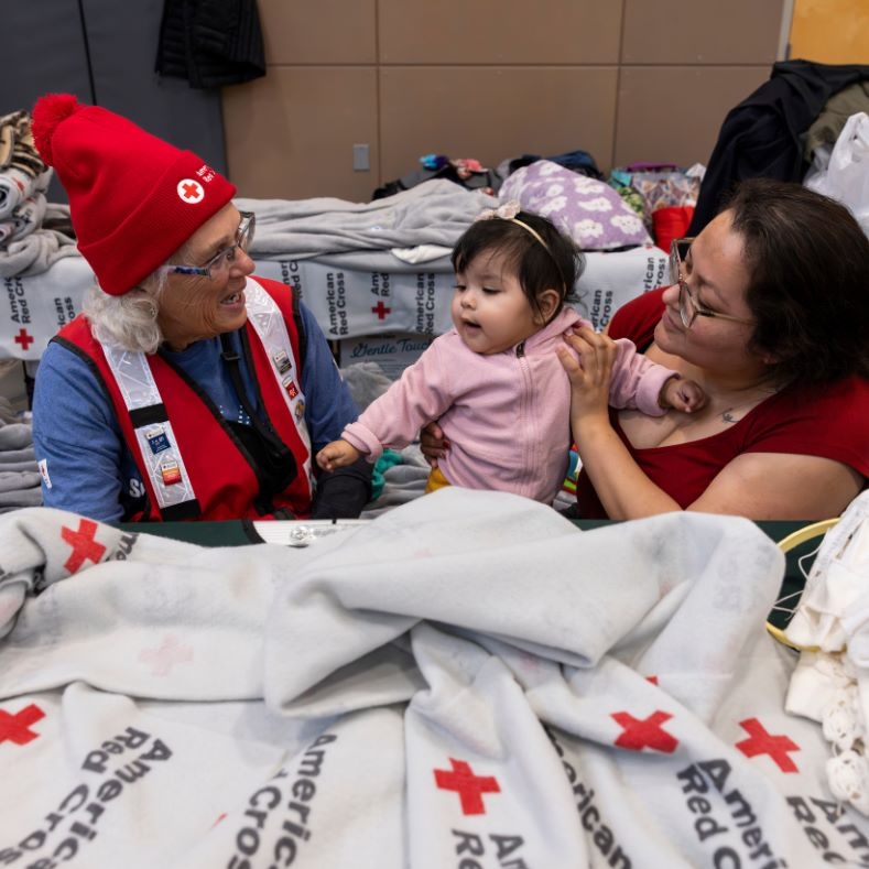 Red Cross volunteer talking to mother an baby in a Red Cross shelther. 