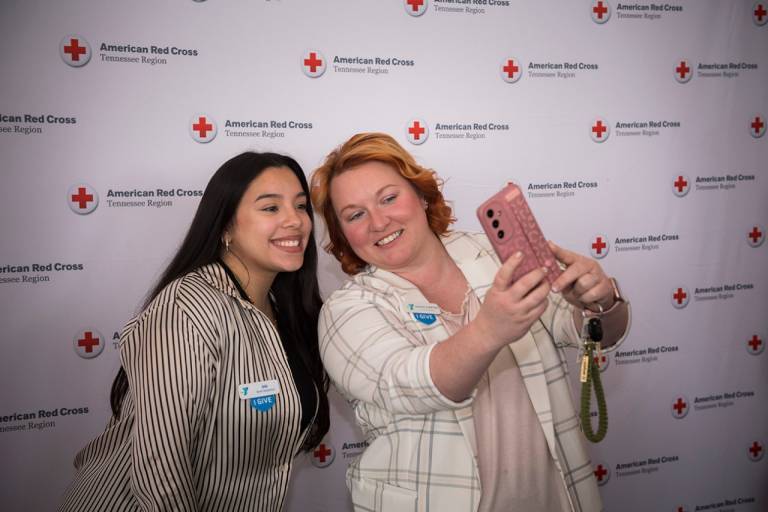 two women taking a picture of themselves with red cross background