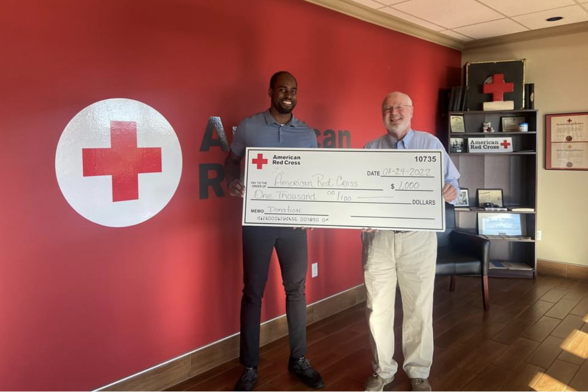Two men stand in Red Cross office holding large check