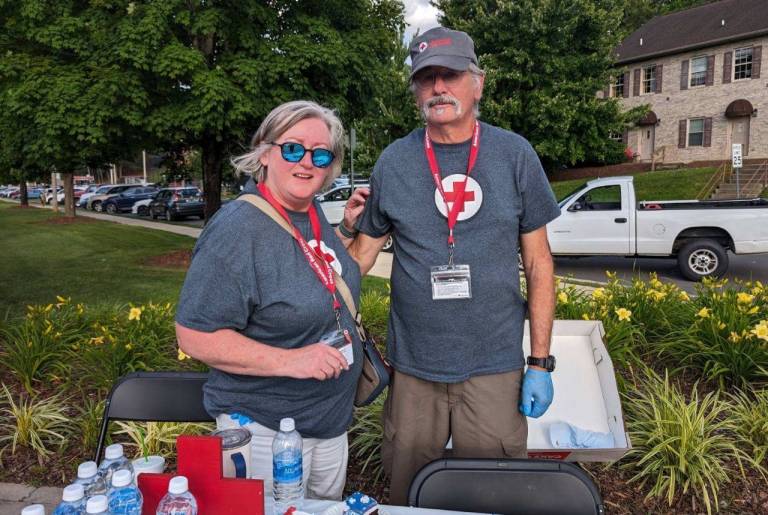 Man and woman in Red Cross branding hand out water