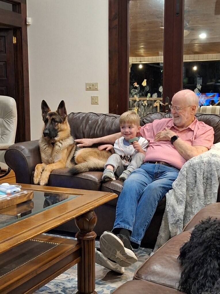 John sits on the couch with young boy and German Shepherd dog