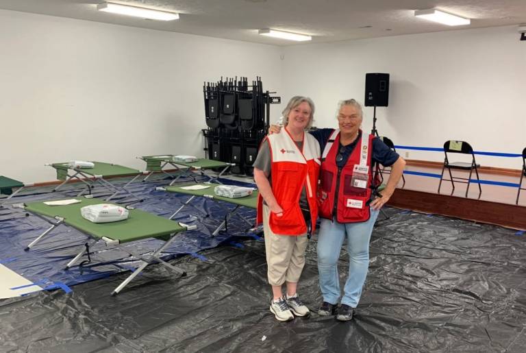 Two red cross volunteers stand in shelter.