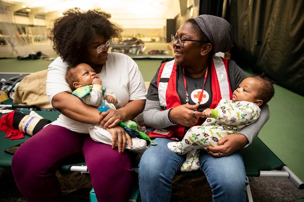 A woman and a Red Cross volunteer holding babies at a shelter