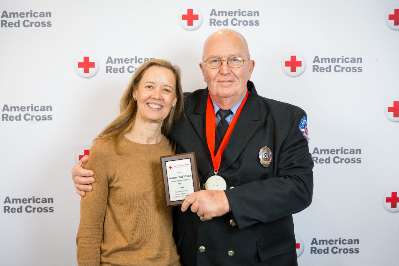 Two people posing for a picture, hugging each other with one holding an award